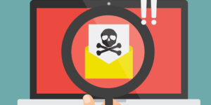 Human hand with magnifying glass found spam email with skull and cross bones computer virus on laptop computer. ZLoader attack